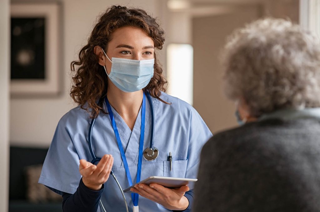 Nurse in a mask talking to an elderly patient