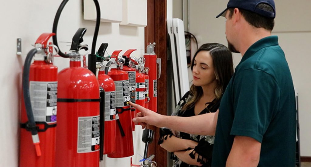 Man pointing to a fire extinguisher as a young woman watches